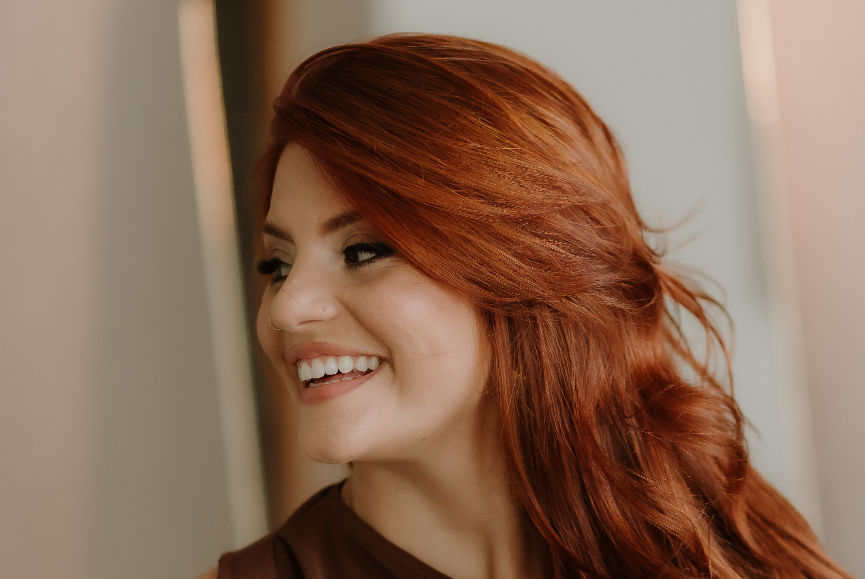 Retrato de Lais sorrindo em close, com cabelo ruivo e luz suave.
